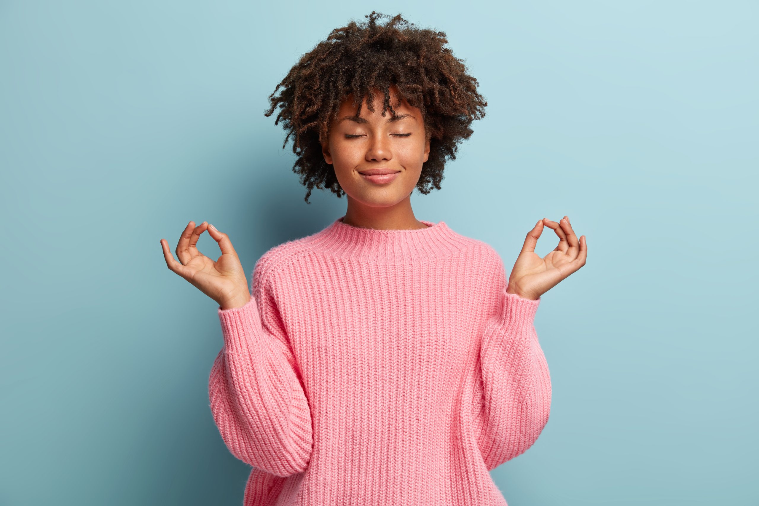 People, peace and meditation concept. Calm black young woman practices yoga indoor, shows okay sign with both hands, demonstrates approval, wears pink clothing, isolated over blue background Le contrat d’entretien À CIEL OUVERT